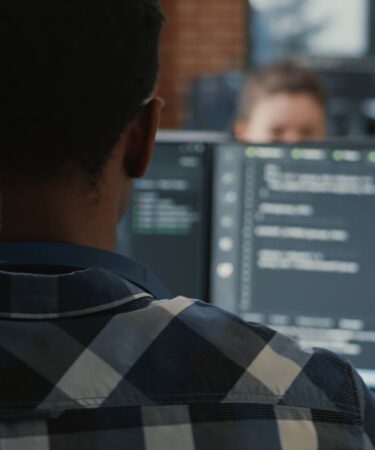 Desenvolvedor trabalhando em frente a monitores com código em ambiente corporativo, demonstrando atividades de Engenharia de Software para Dispositivos Móveis.
