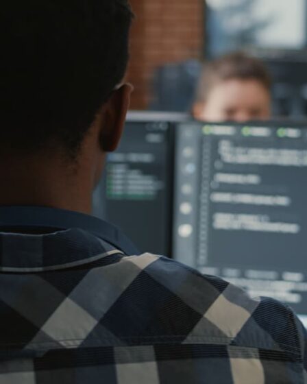 Desenvolvedor trabalhando em frente a monitores com código em ambiente corporativo, demonstrando atividades de Engenharia de Software para Dispositivos Móveis.