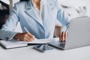 Profissional trabalhando em notebook enquanto faz anotações em caderno durante análise de processos e documentos relacionados ao Direito Administrativo.