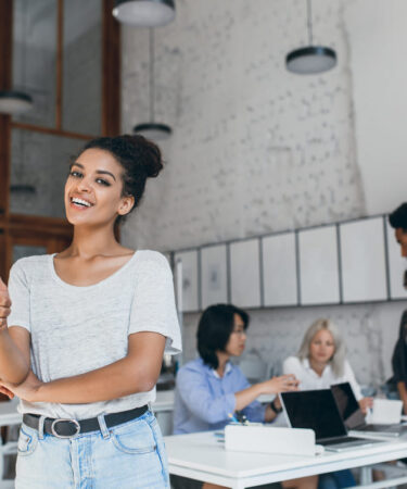 Profissional em ambiente de trabalho usando notebook com colegas ao fundo, mostrando que quem faz pós-graduação pode estagiar.