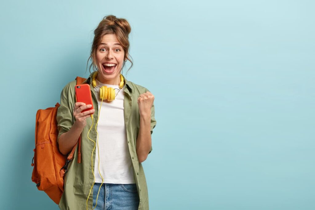 Jovem comemorando a Black Friday da Uninter com celular, fones de ouvido e mochila.