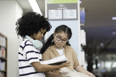 Duas crianças leem o mesmo livro simultaneamente.